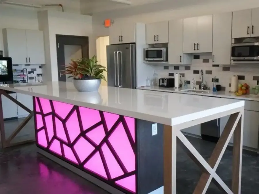 Office kitchen island with a backlit pink geometric panel and white countertop