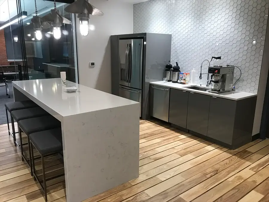 Office kitchen with white waterfall island, gray cabinets and hexagon tile wall