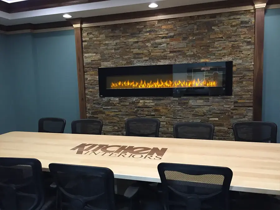 Conference room table inlaid with the Kitchen Interiors logo before a stone fireplace wall
