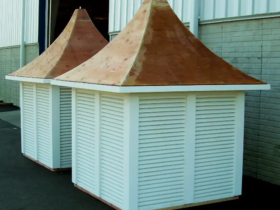 Two louvered cupolas with flared roofs awaiting finish outside a shop
