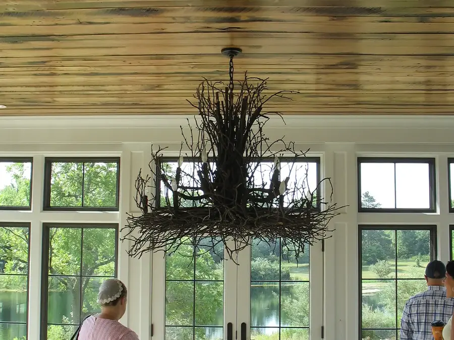 Rustic twig chandelier hanging from a plank ceiling in a room of tall windows