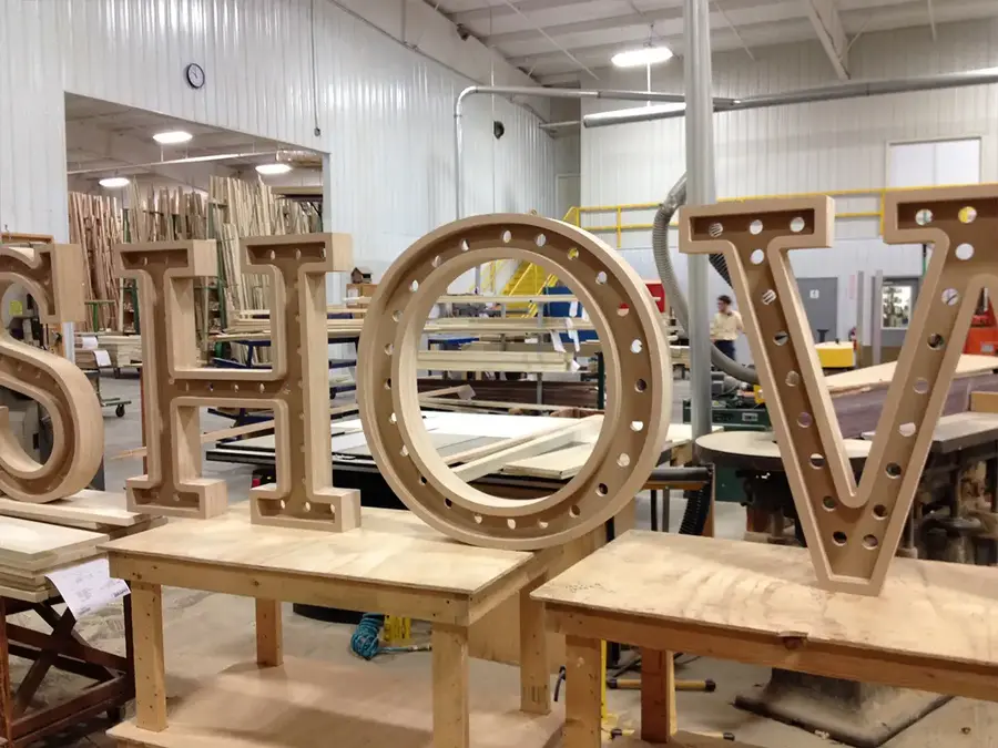 Large wooden marquee letters with bulb holes being built in a millwork shop