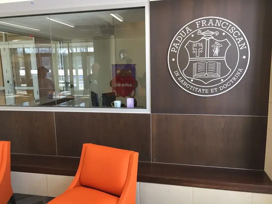 Padua Franciscan crest on wood-grain wall panels above orange lounge chairs