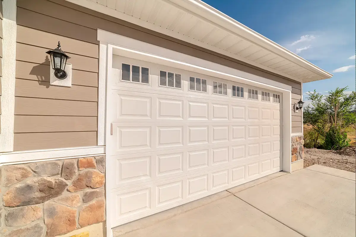 White raised-panel garage door with window lites on a home with lap siding and stone