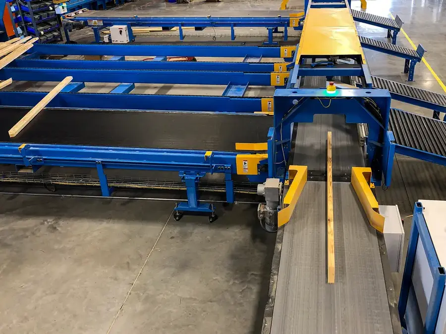 Blue and yellow automated conveyor system moving a board through a truss plant