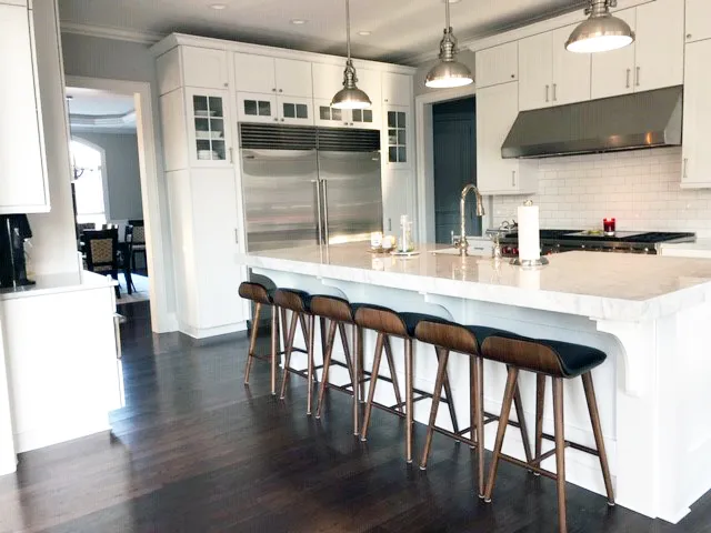 White kitchen with marble island, wood and leather stools and industrial pendants