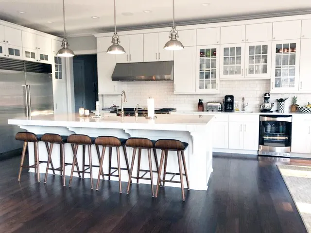 White kitchen with long island, wood bar stools and stainless dome pendants