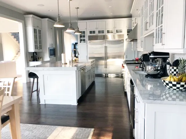 Long white kitchen with marble countertops, glass-front uppers and built-in refrigerator