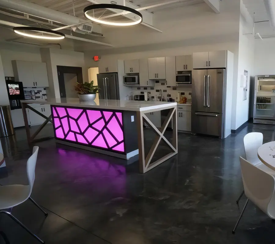 Office break room with a backlit pink kitchen island and stainless refrigerators