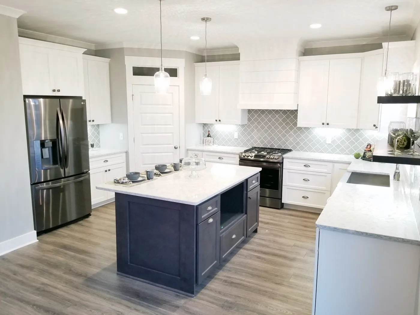White kitchen with dark gray island, stone countertops and gray arabesque tile