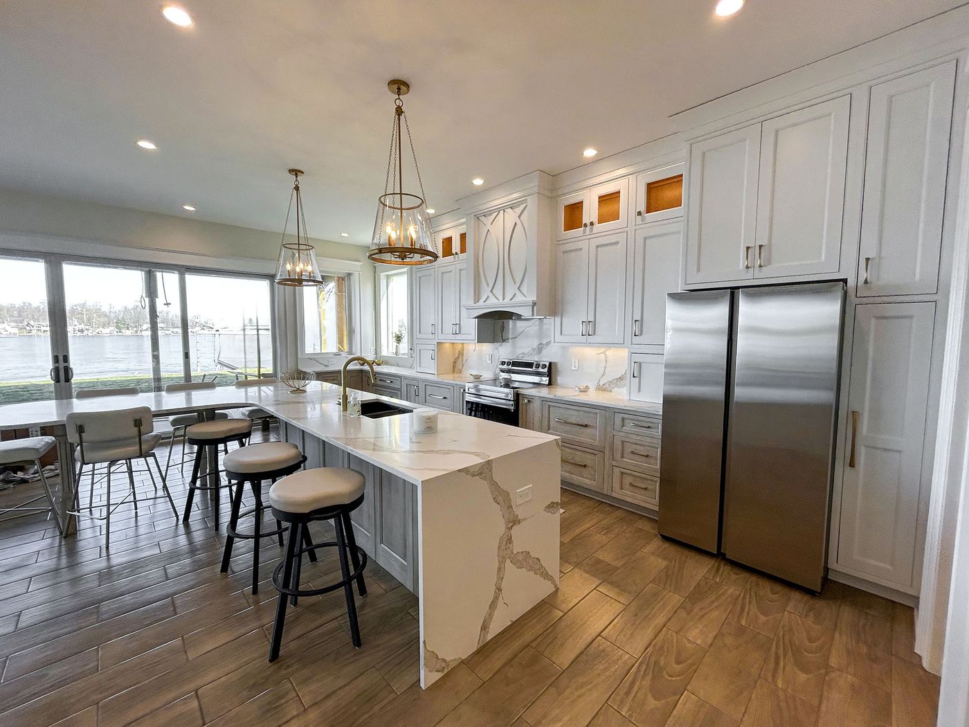 White kitchen with waterfall island, bar stools and lantern pendants near waterfront windows