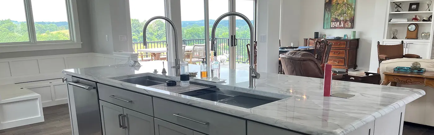Gray kitchen island with two sinks and tall faucets, overlooking a deck and green hills