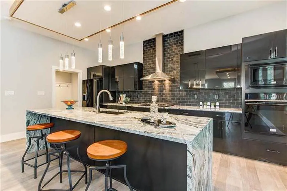 Glossy black kitchen with marble waterfall island, subway tile wall and leather stools