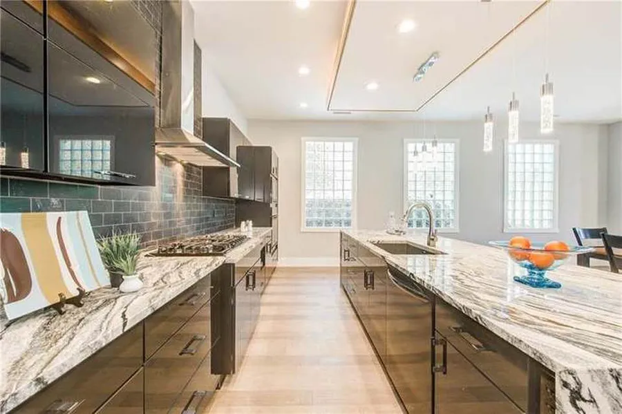 Galley view of glossy black cabinets, marble countertops and glass block windows