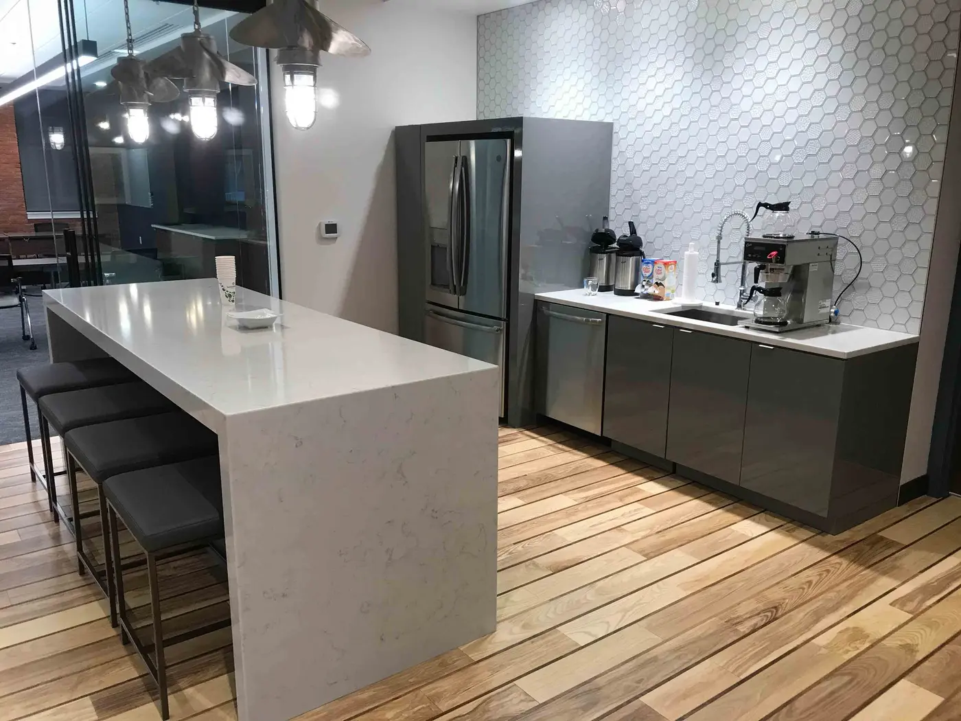 Office break room with gray cabinets, hex tile wall and stone waterfall island