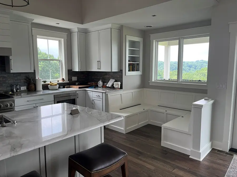 White kitchen with built-in corner bench seating under windows overlooking wooded hills
