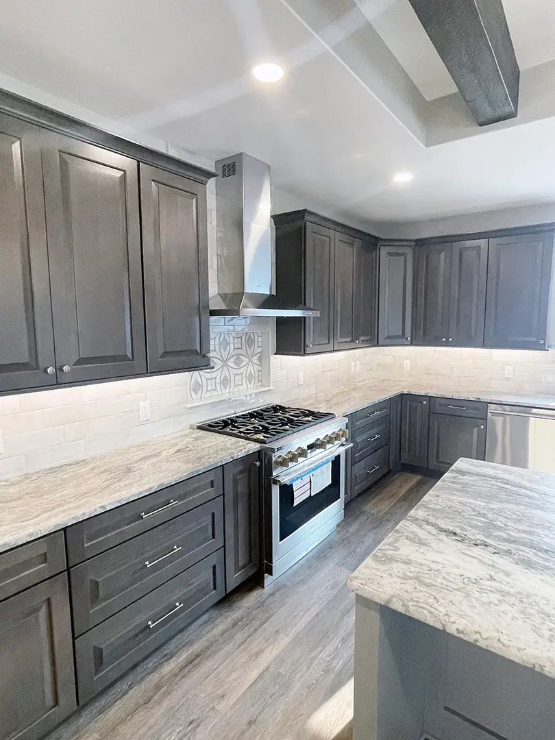 Dark gray raised-panel cabinets with granite counters and a stainless range and hood