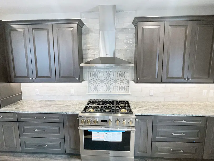 Stainless range and chimney hood framed by dark gray cabinets and patterned tile inset