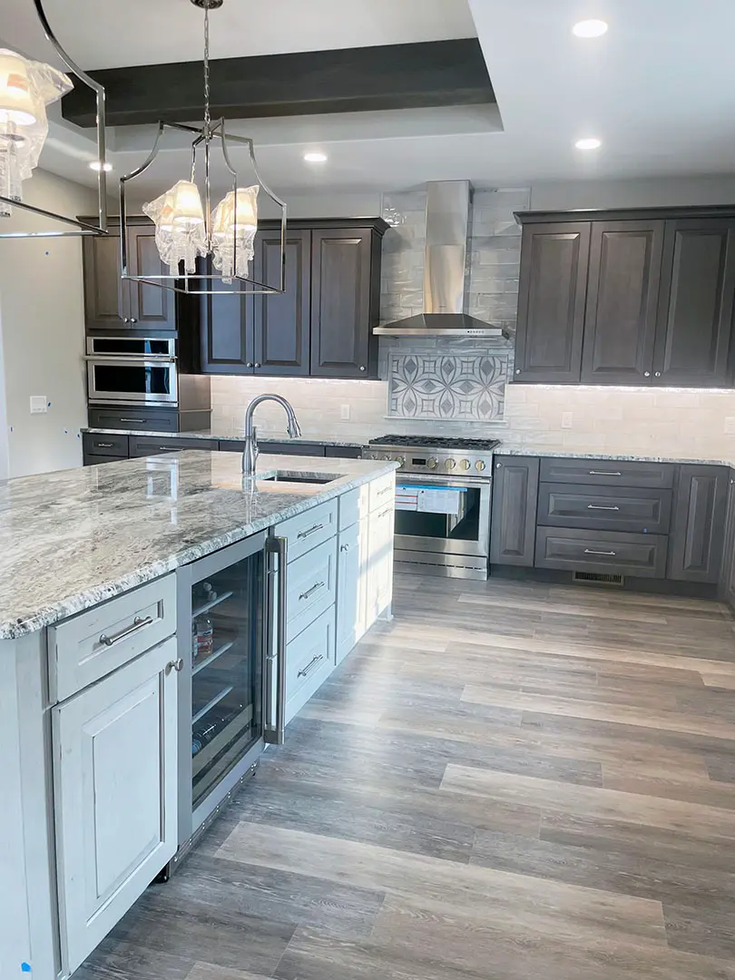 Light gray island with beverage fridge and granite top facing dark gray cabinetry