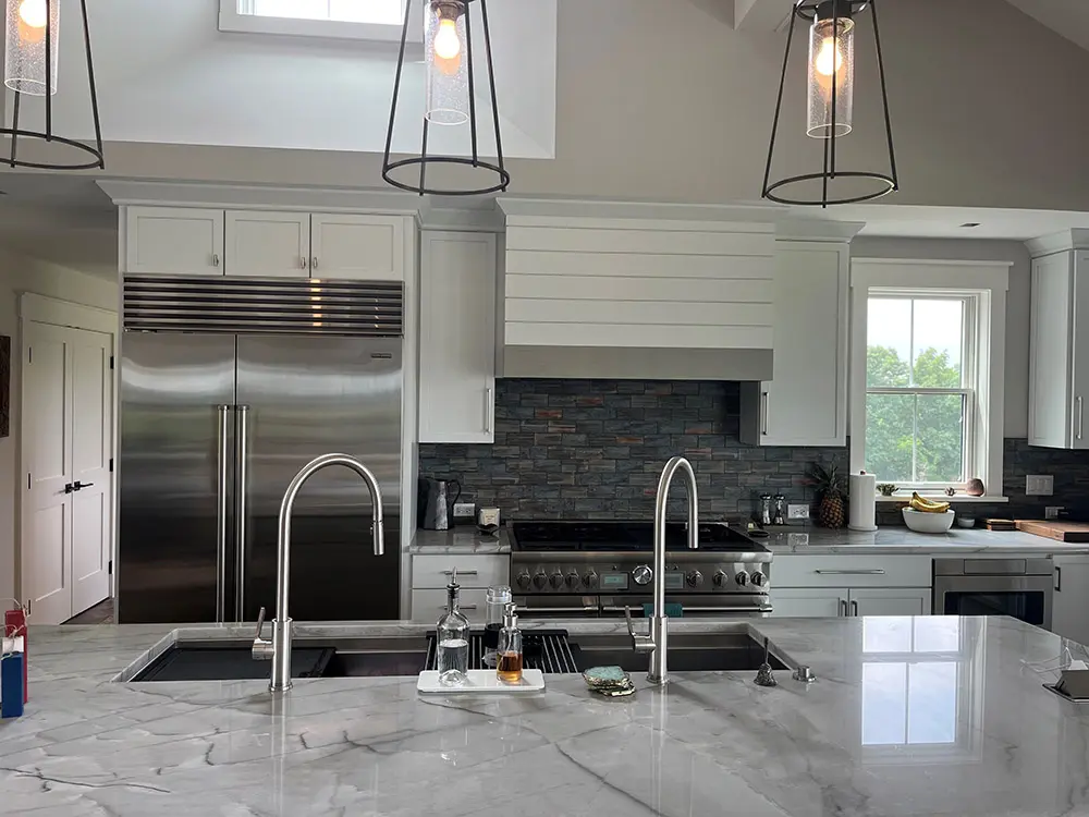 Marble-look island with two sinks facing white cabinets, slate tile and a stainless range