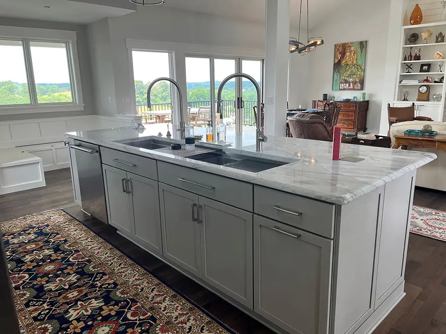 Light gray island with double sink and marble-look top, open to living room