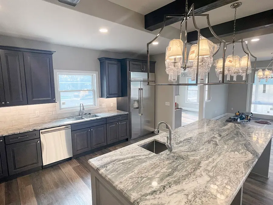 Dark gray cabinets with a swirled granite island and silver lantern chandeliers