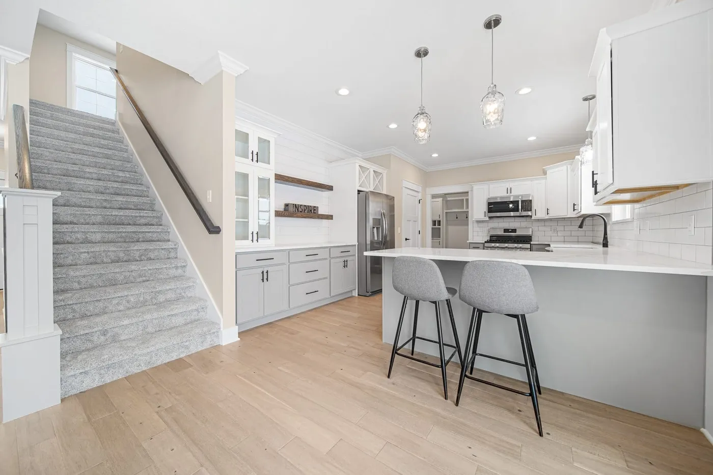 White and gray kitchen with stone peninsula, gray stools and open stairway
