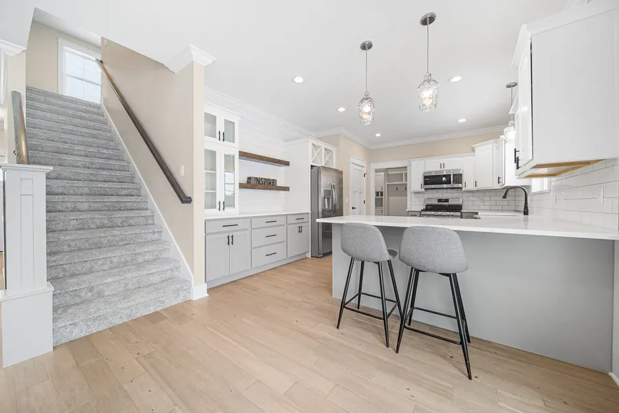 White and gray kitchen with stone peninsula, gray stools and open stairway