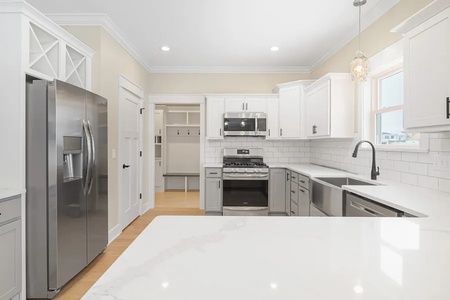 White and gray kitchen seen across a stone peninsula toward a mudroom