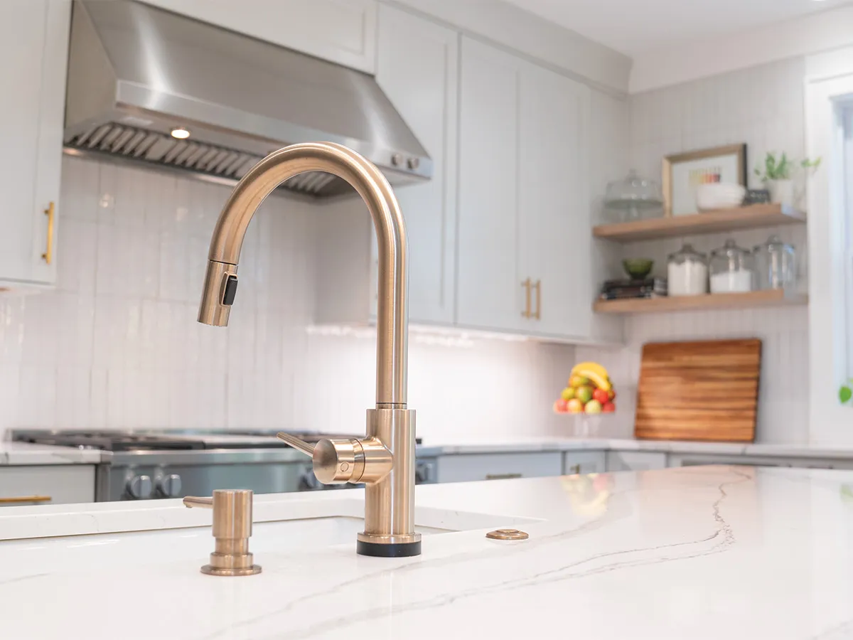 Champagne bronze faucet on a white veined island countertop in a white kitchen
