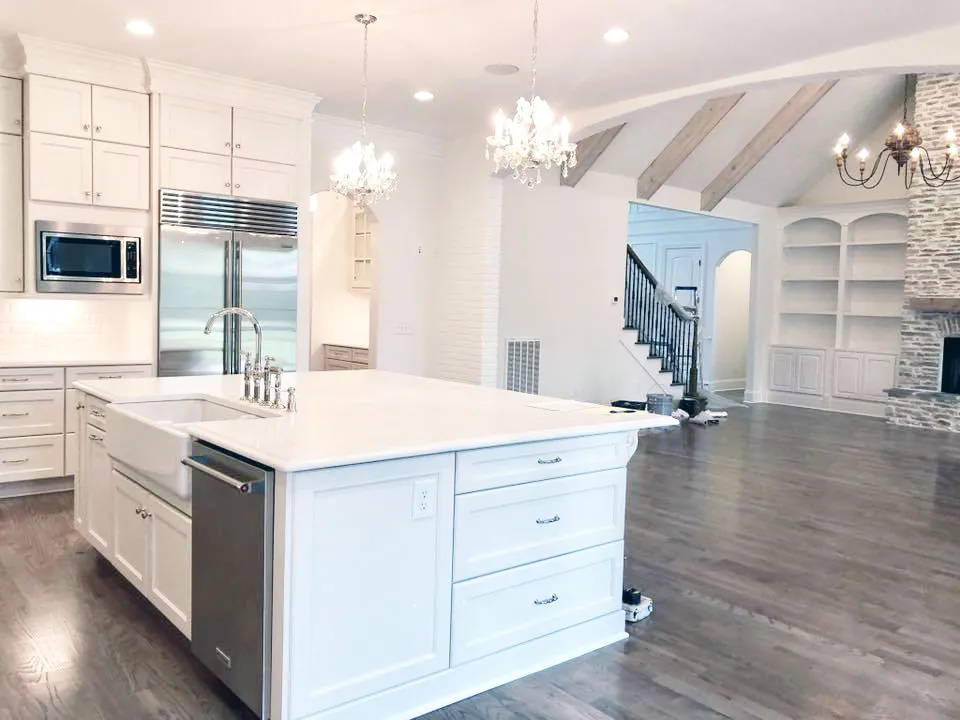 White kitchen with farmhouse sink island, crystal chandeliers and open living area