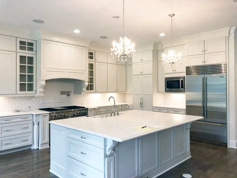 White kitchen with large painted island, crystal chandeliers and built-in refrigerator