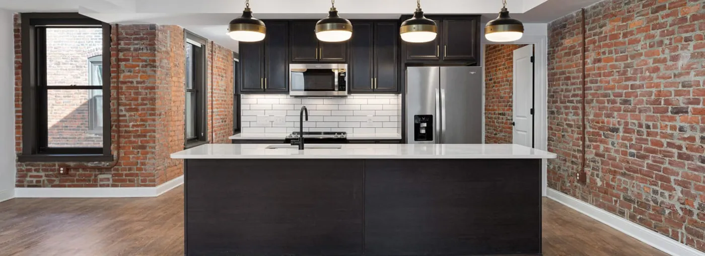 Apartment kitchen with black cabinets, white subway tile, island and exposed brick walls