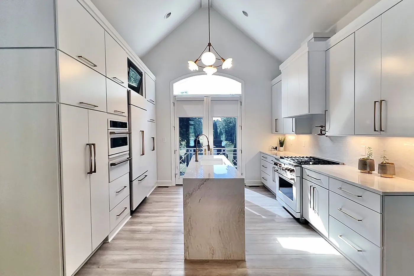 Galley kitchen with white flat-panel cabinets, waterfall stone island and vaulted ceiling