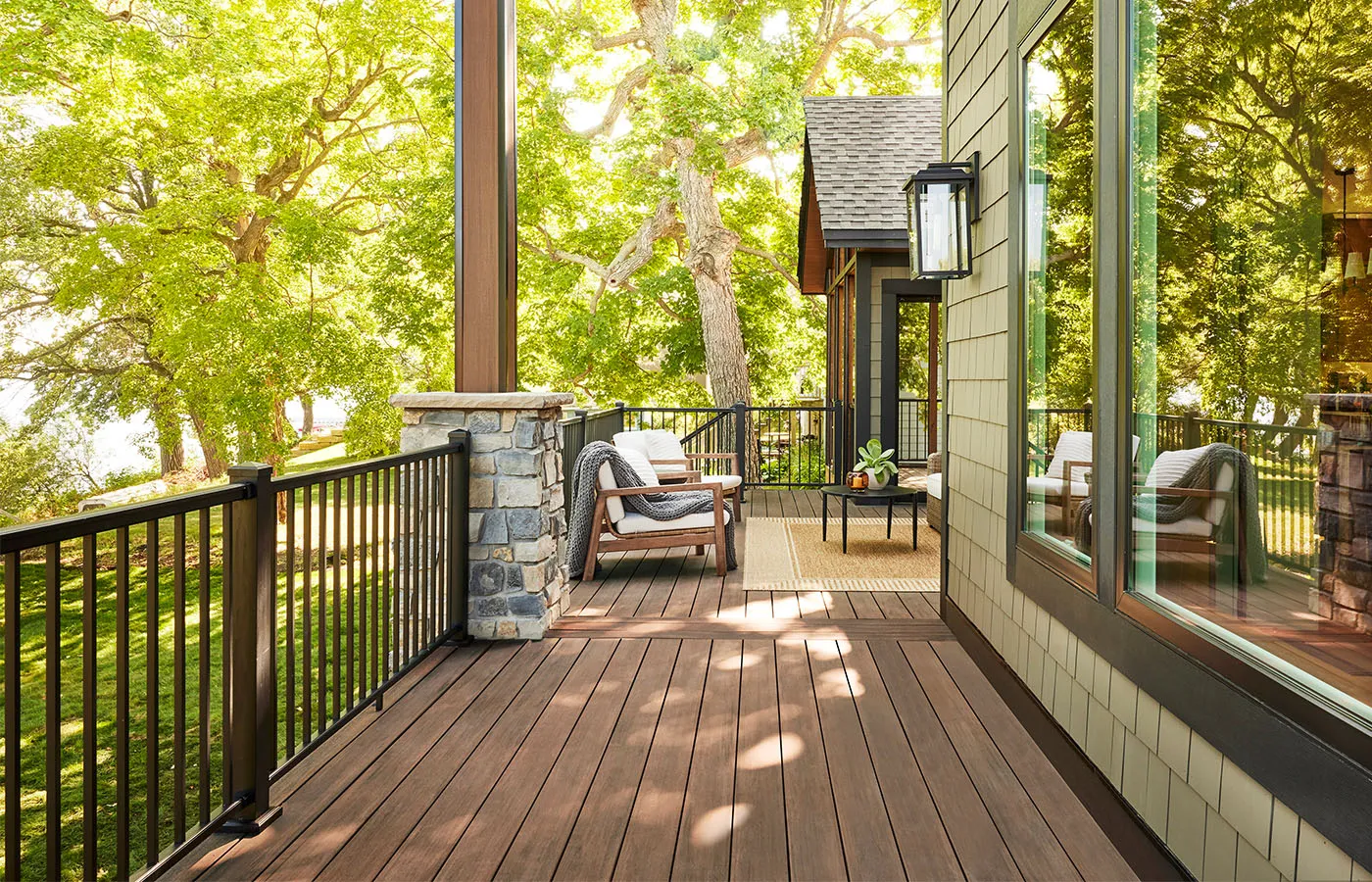 Covered composite deck with black metal railing, stone pillar and lounge chairs under shade trees