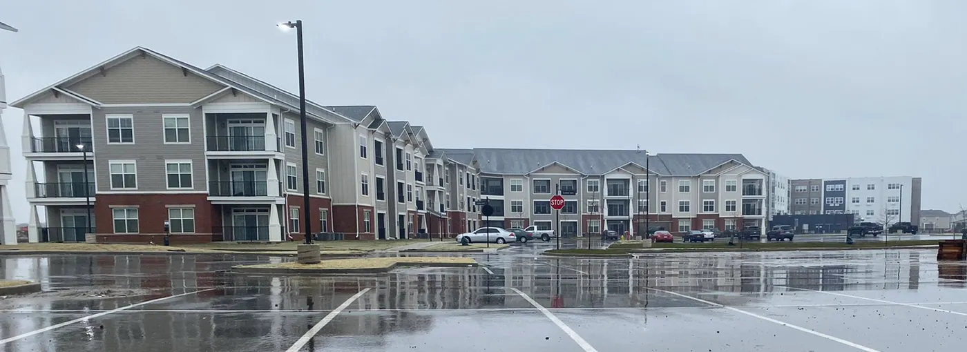 Three-story apartment buildings across a wet parking lot on an overcast day