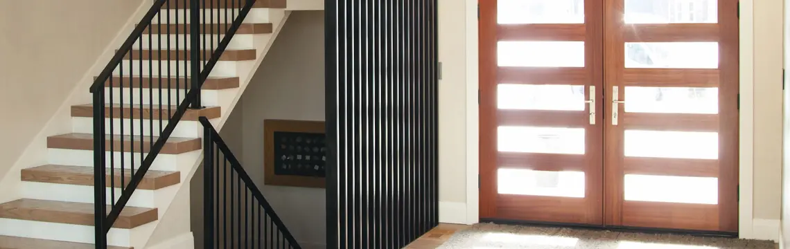 Entry with wood double doors with frosted glass lites beside a staircase with black metal railing