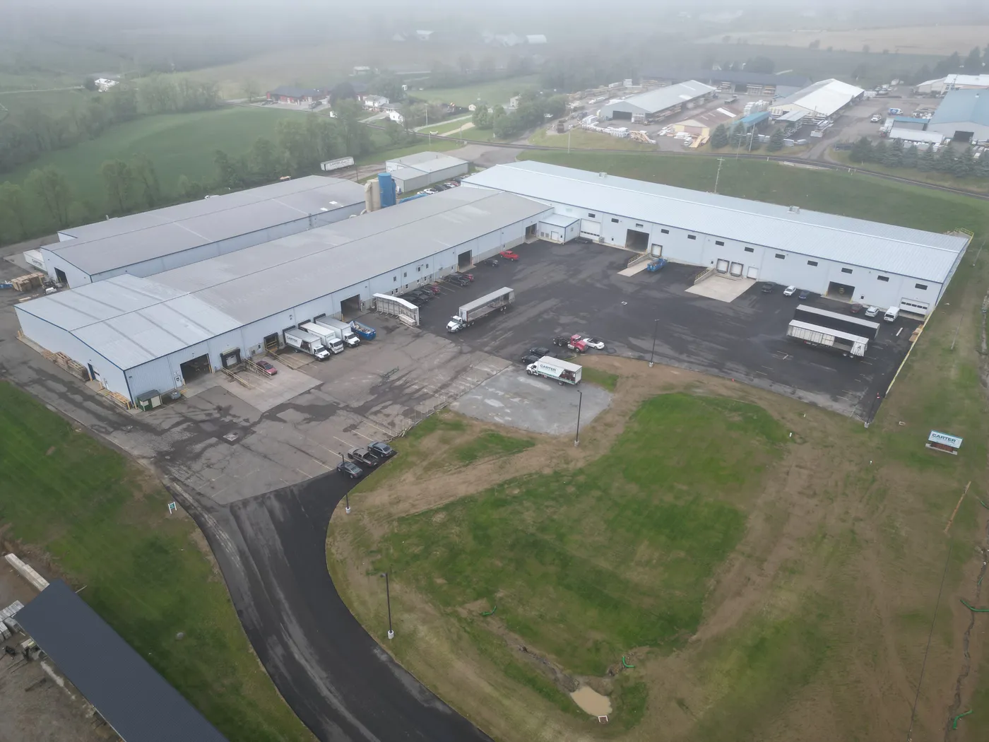 Aerial view of large metal manufacturing buildings and a truck lot on a foggy morning