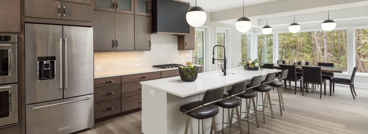 Open kitchen with dark cabinets, white island with bar stools and globe pendants by a dining area