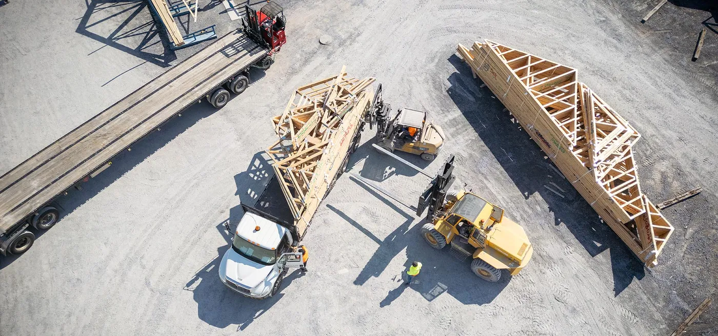 Overhead view of forklifts loading roof trusses onto a flatbed truck