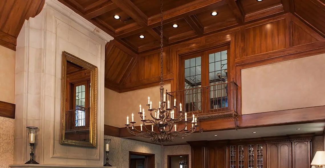 Great room with coffered wood ceiling, wood-paneled balcony, stone fireplace and candle chandelier