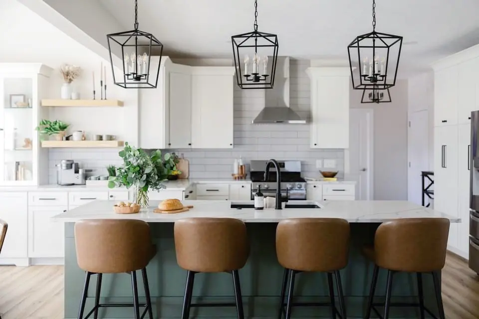White kitchen with sage green island, leather bar stools and black lantern pendants