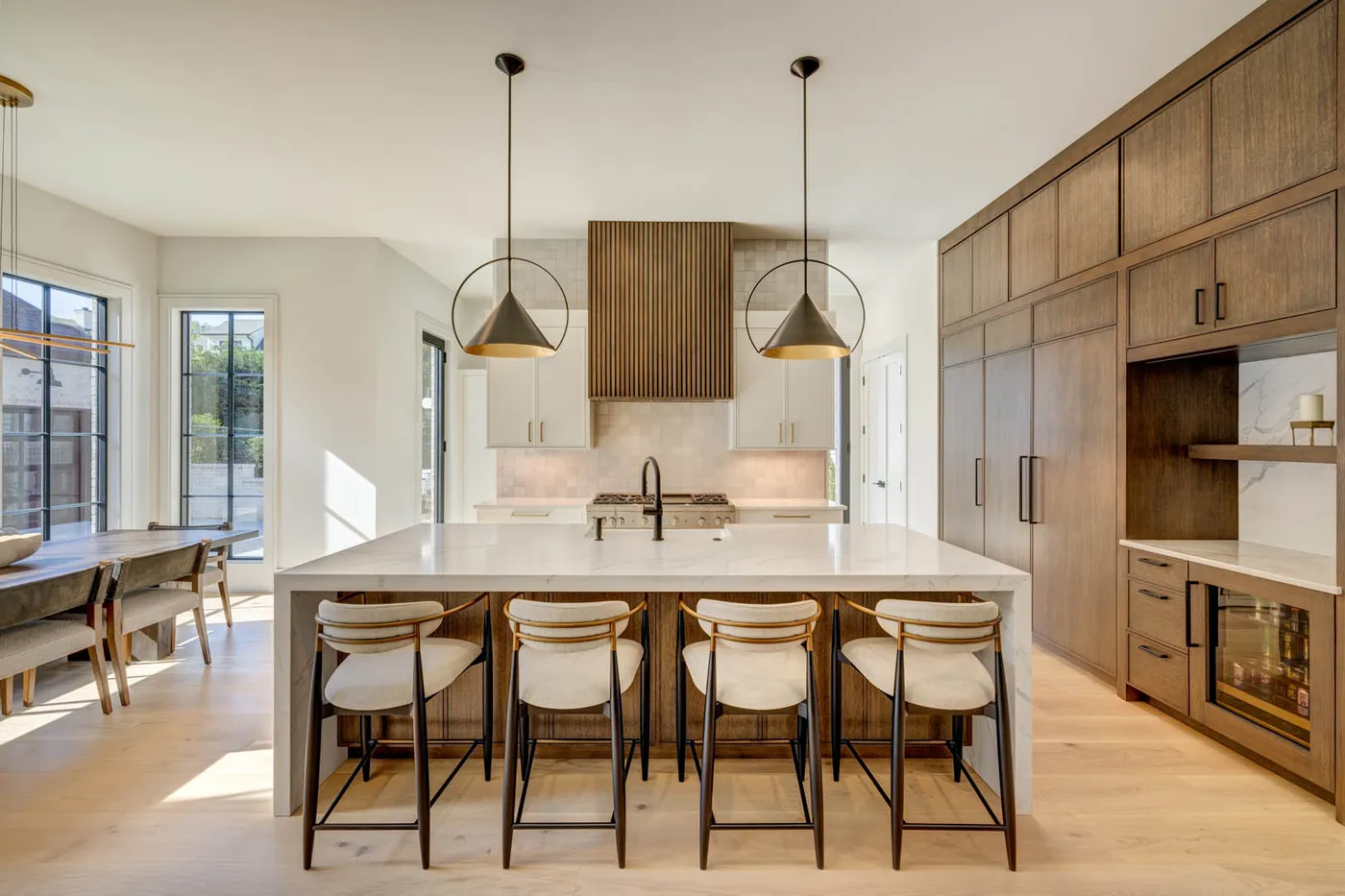 Kitchen with white island, cream bar stools, dome pendants and wood-paneled range hood