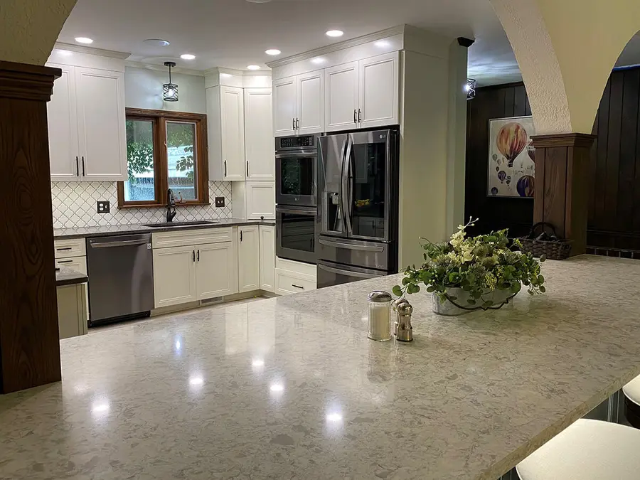 White kitchen with stainless appliances and a large speckled stone peninsula