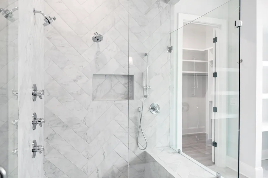 Glass-enclosed walk-in shower with white herringbone marble tile and a built-in niche