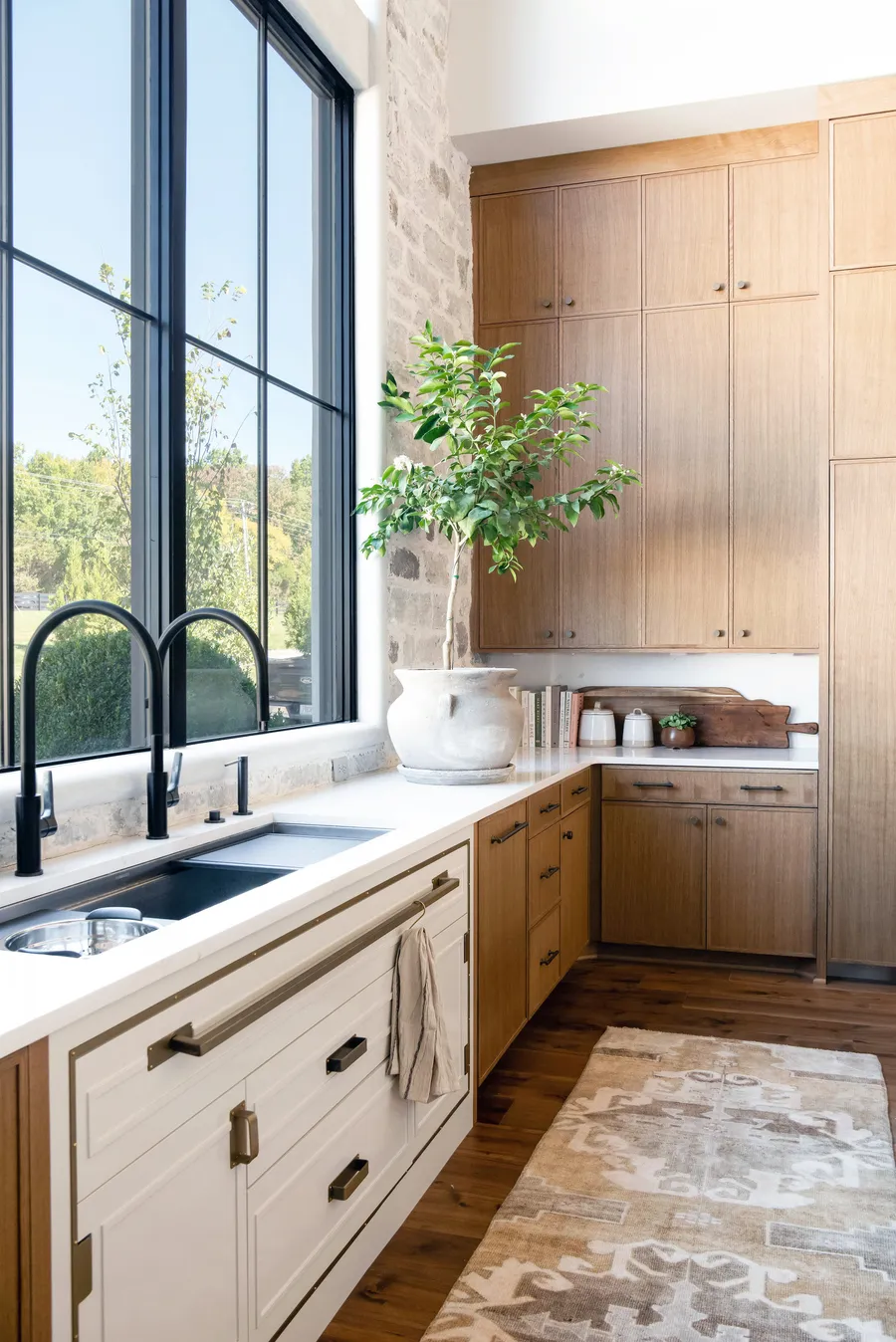Light wood cabinets beside white sink cabinets under tall black-framed windows