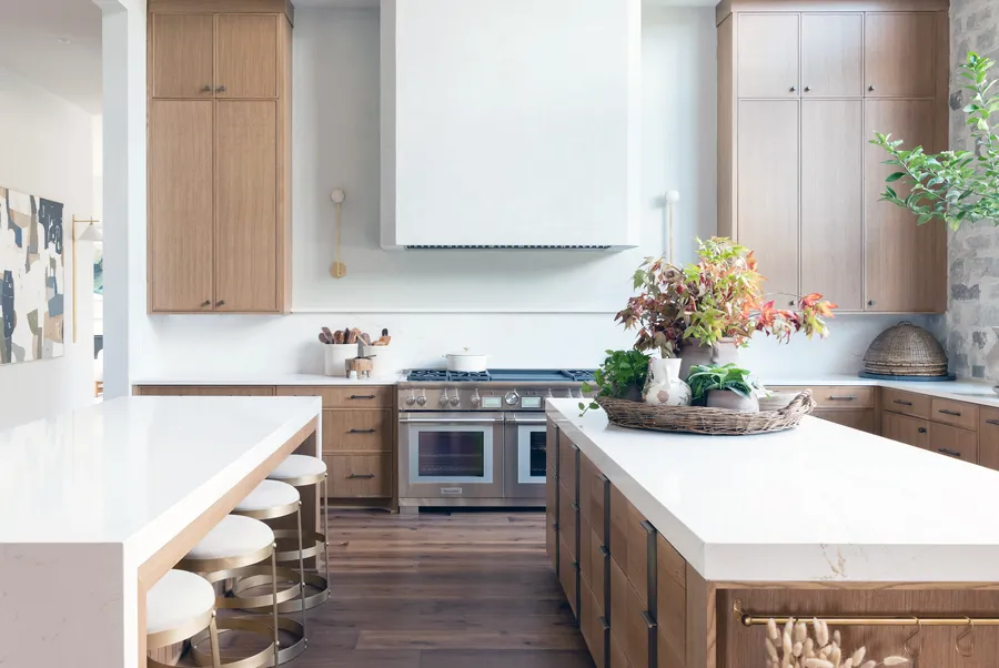 Two white-topped islands with wood bases and brass stools facing a white plaster hood