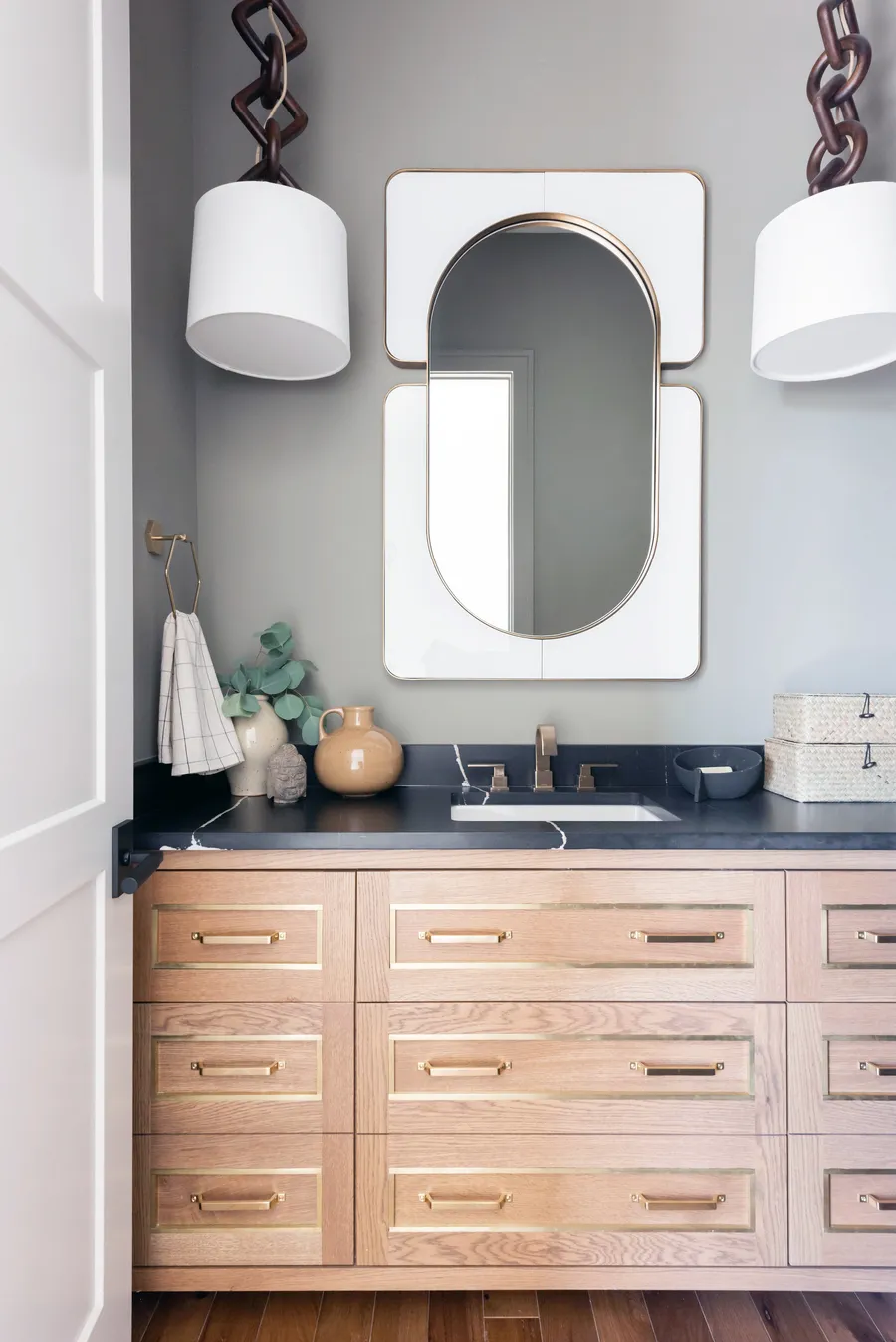 Light wood vanity with brass-inlaid drawers, black counter and white drum pendants