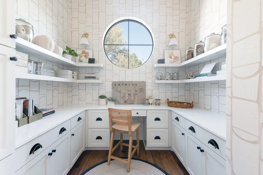 Pantry office nook with white cabinets, open shelves, desk and round window