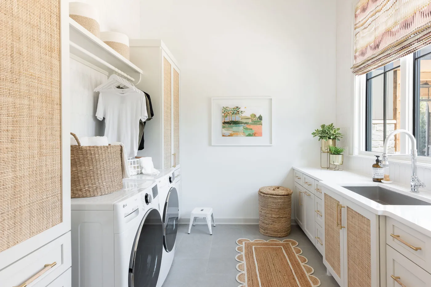 Bright laundry room with woven cabinet doors, washer and dryer, sink and hanging rod